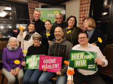 Eine Gruppe von Menschen, die vor einem Banner der GRÜNEN stehen und sitzen. 